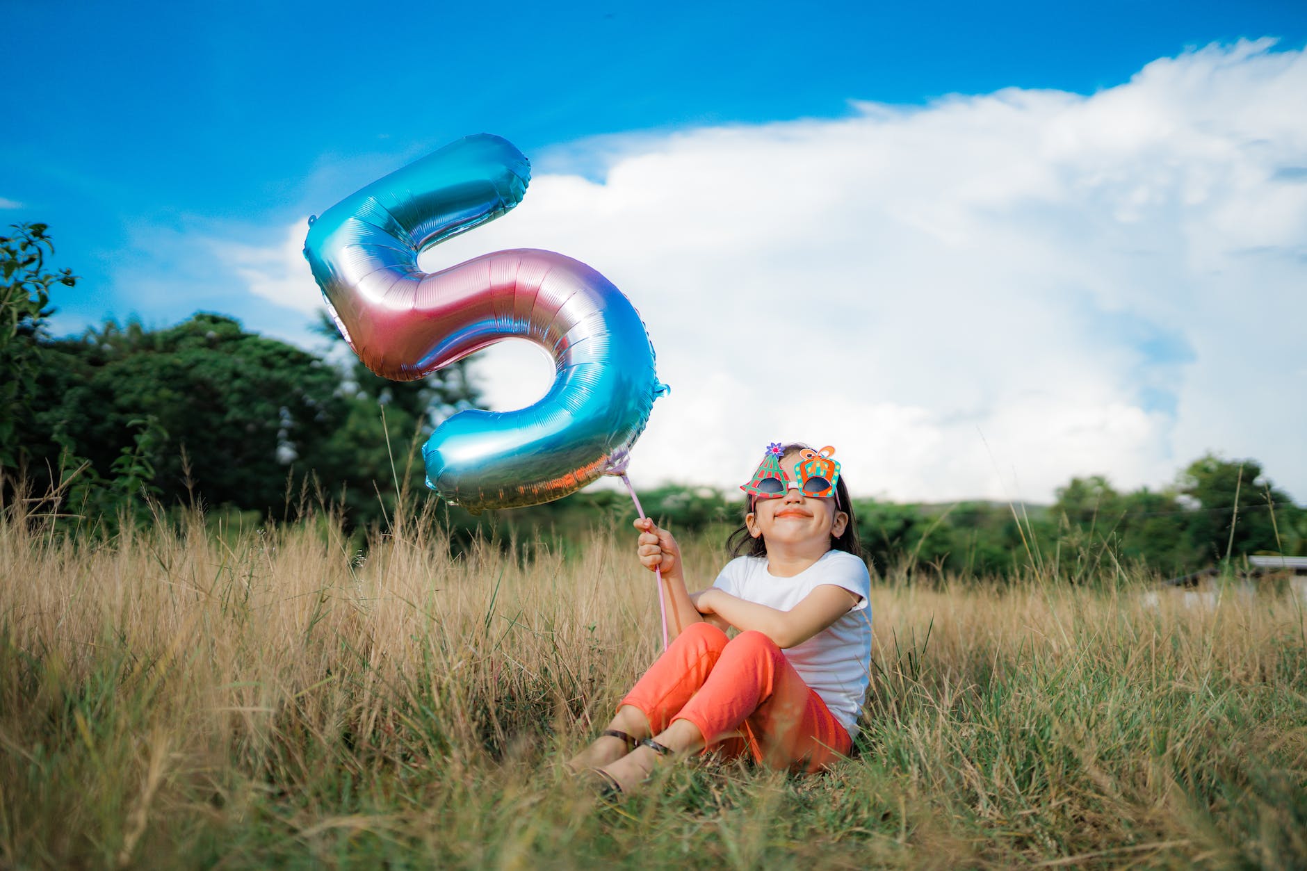 girl holding a balloon while sitting on grass